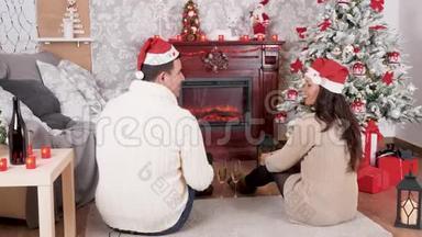 在圣诞节装饰的房间里，<strong>一对情侣</strong>坐在壁炉前的地板上